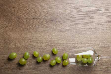 Wineglass with scattered grapes on wooden table, flat lay. Space for textの写真素材