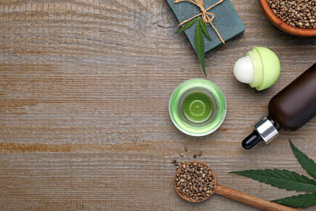 Hemp cosmetics and green leaves on wooden table, flat lay. Space for textの写真素材