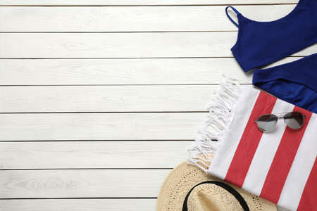 Beach towel, swimsuit, sunglasses and hat on white wooden background, flat lay. Space for textの写真素材