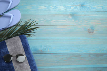 Beach towel, flip flops and sunglasses on light blue wooden background, flat lay. Space for textの写真素材