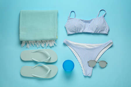 Beach towel, swimsuit, flip flops and sunglasses on light blue background, flat layの写真素材