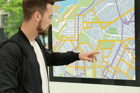 Young man near public transport map at bus stop, closeup
