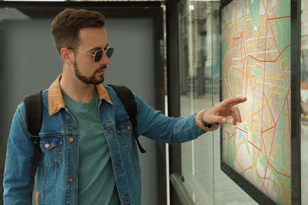 Young man with backpack near public transport map at bus stop