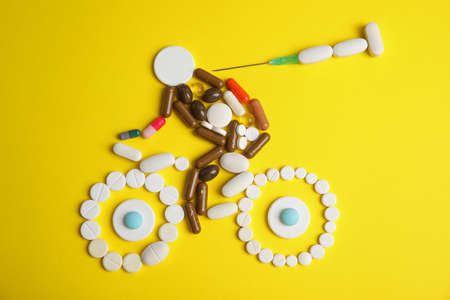 Sportsman, bike and syringe made of pills on yellow background, flat lay. Using doping in cycling sport conceptの写真素材