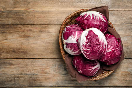 Fresh ripe radicchios in wicker basket on wooden table, top view. Space for textの写真素材