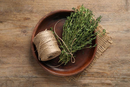Bunch of aromatic thyme and twine in bowl on wooden table, top viewの写真素材