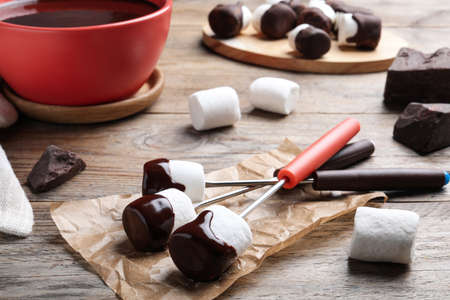 Delicious marshmallows covered with chocolate on wooden table