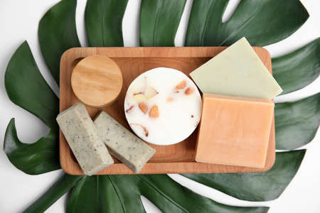 Wooden tray with eco friendly personal care products on green leaf, top view