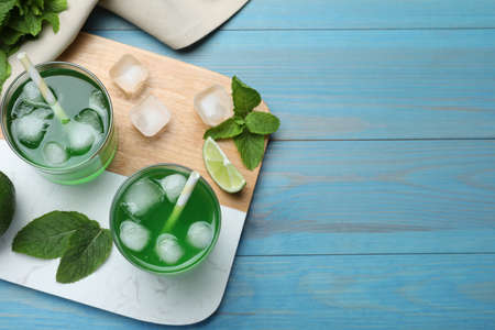 Delicious mint liqueur with green leaves and ice cubes on turquoise wooden table, flat lay. Space for textの写真素材