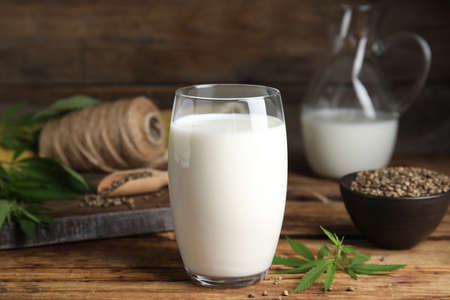 Glass of fresh hemp milk, seeds and leaves on wooden tableの写真素材