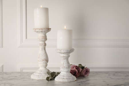 Elegant candlesticks with burning candles and flowers on white marble tableの写真素材