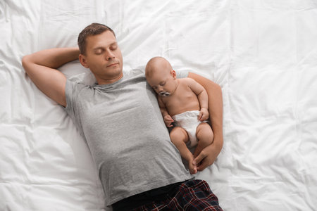 Father and baby sleeping on bed together, top viewの写真素材
