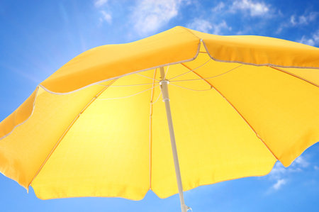 Open big yellow beach umbrella and beautiful blue sky with white clouds on background