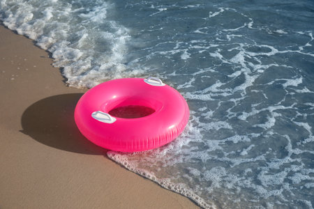 Bright pink inflatable ring on sandy beach near sea