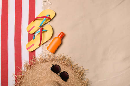 Beach towel, hat, sunglasses, sunscreen and flip flops on sand, flat lay. Space for textの写真素材