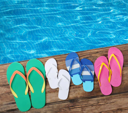 Pairs of flip flops on wooden deck near swimming pool, flat lay