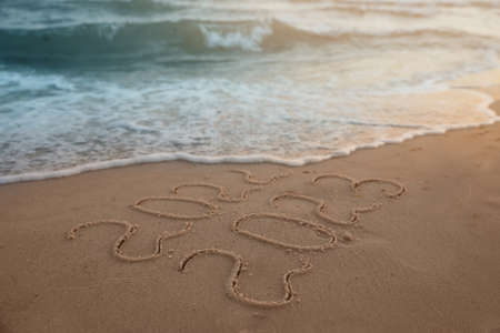 Sea wave rolling onto sandy beach with written 2022 and 2023. New Yearの写真素材