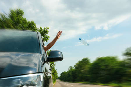 Driver throwing away plastic bottle from car window. Garbage on roadの写真素材