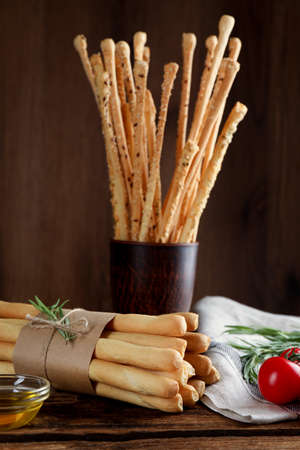 Delicious grissini sticks, oil, rosemary and tomatoes on wooden table