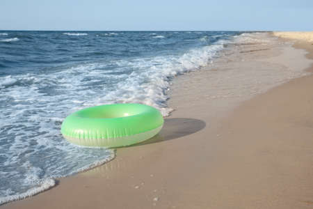 Green inflatable ring on sandy beach near sea, space for textの写真素材