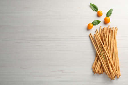 Delicious grissini sticks, basil leaves and yellow tomatoes on white wooden table, flat lay. Space for textの写真素材