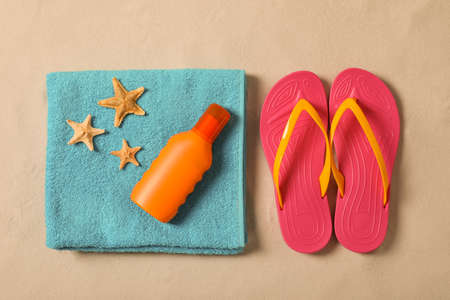Beach towel, sunscreen, starfishes and flip flops on sand, flat layの写真素材