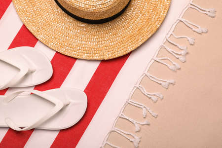 Beach towel, hat and flip flops on sand, flat lay
