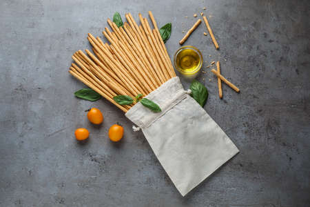 Delicious grissini sticks, basil leaves, cherry tomatoes and oil on gray table, flat layの写真素材
