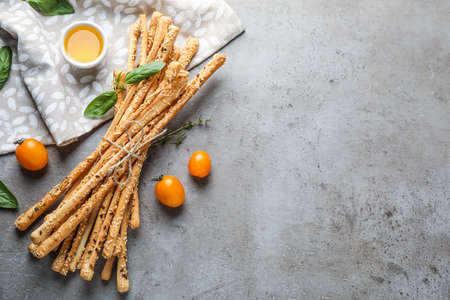 Delicious grissini sticks, oil, tomatoes and basil leaves on gray table, flat lay. Space for textの写真素材