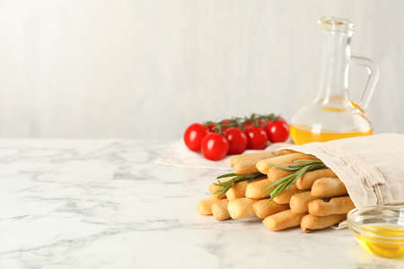 Delicious grissini sticks, oil, rosemary and tomatoes on white marble table. Space for textの写真素材