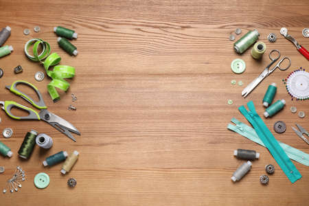 Flat lay composition with different sewing accessories on wooden background. Space for text
