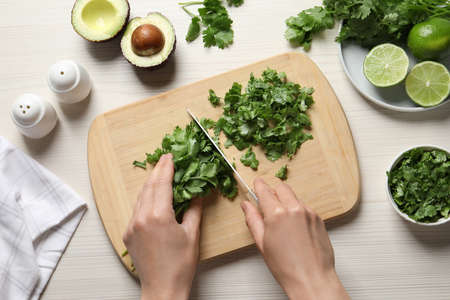Woman cutting fresh green cilantro at white wooden table, top viewの写真素材