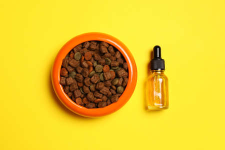 Glass bottle of tincture near bowl with dry pet food on yellow background, flat layの写真素材