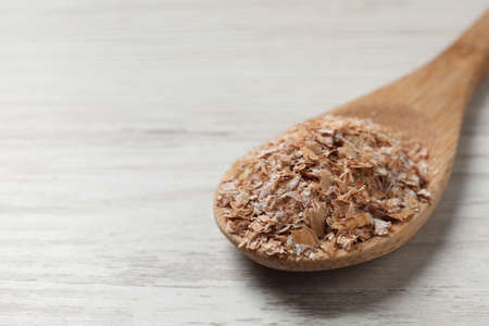 Spoon of wheat bran on white wooden table, closeup. Space for text