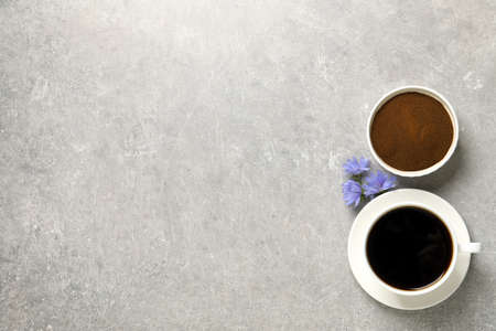 Cup of delicious chicory drink, powder and flowers on light gray table, flat lay. Space for text