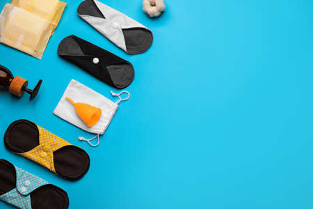 Cloth menstrual pads and other female hygiene products on light blue background, flat lay. Space for...