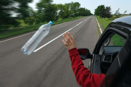 Driver throwing away plastic bottle from car window. Garbage on roadの写真素材