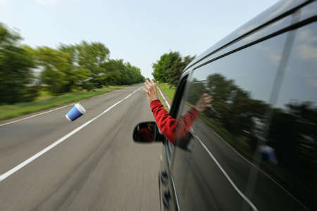 Driver throwing away paper coffee cup from car window. Garbage on roadの写真素材