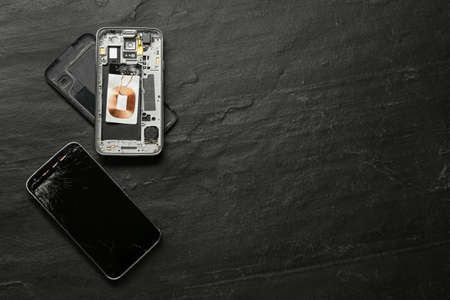 Damaged smartphone on black background, flat lay with space for text. Device repairingの写真素材