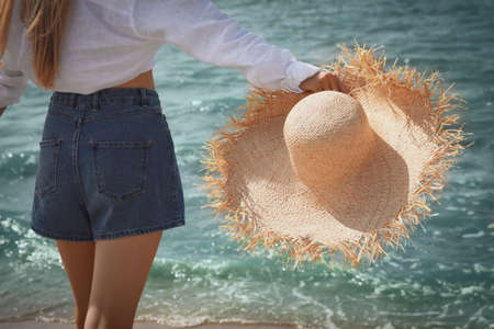Young woman with straw hat near sea on sunny day in summer, closeup back viewの写真素材