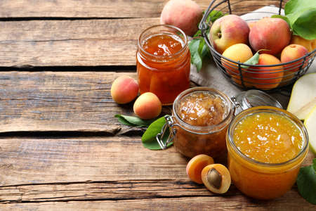 Jars with different jams and fresh fruits on wooden table. Space for textの写真素材