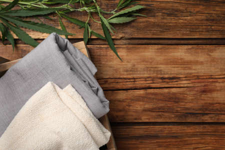 Hemp cloths in crate and green leaves on wooden table, flat lay. Space for textの写真素材