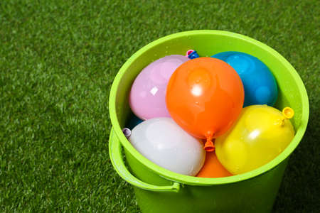 Bucket full of colorful water bombs on green grass, closeup. Space for textの写真素材