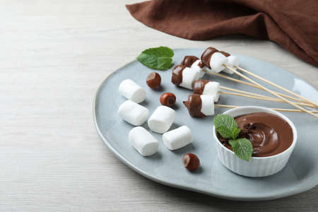 Bowl with melted chocolate and marshmallows on white wooden tableの写真素材