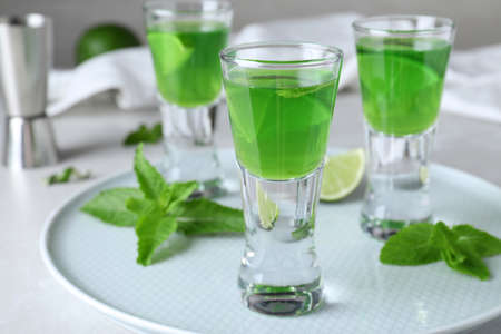 Delicious mint liqueur with lime and green leaves on white table, closeup
