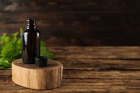 Glass bottle of nettle oil with leaves on wooden table. Space for text