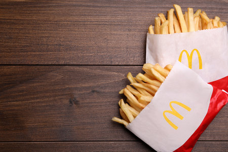 MYKOLAIV, UKRAINE - AUGUST 12, 2021: Two small portions of McDonald's French fries on wooden table,...