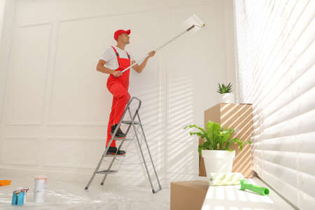 Worker painting wall with roller on ladder indoorsの写真素材