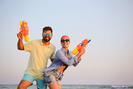 Happy couple with water guns near sea at sunsetの写真素材