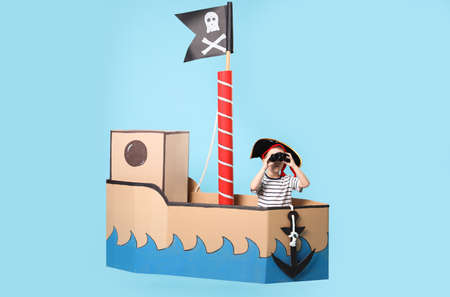Little boy playing with binoculars in pirate cardboard ship on turquoise backgroundの写真素材